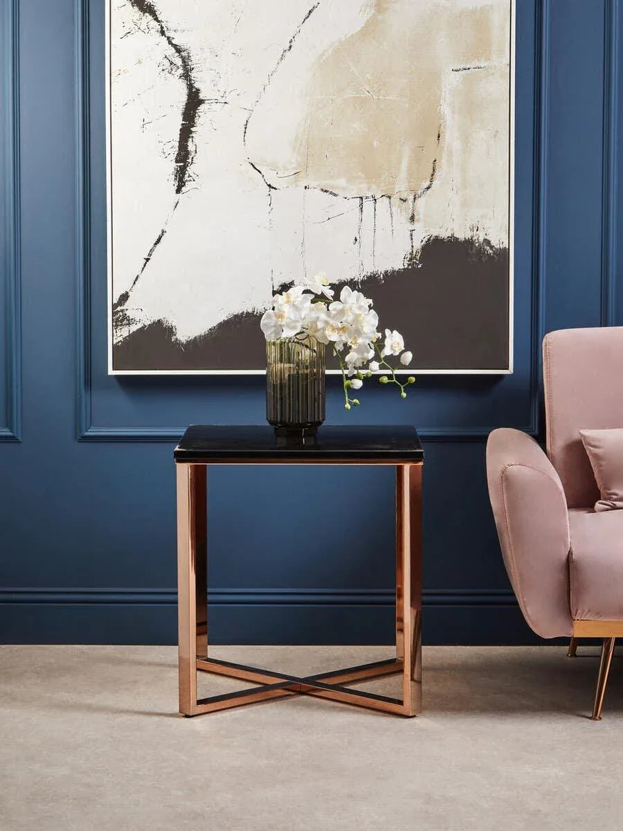 Black glass side table with gold metal legs beside blush armchair and modern art wall decor