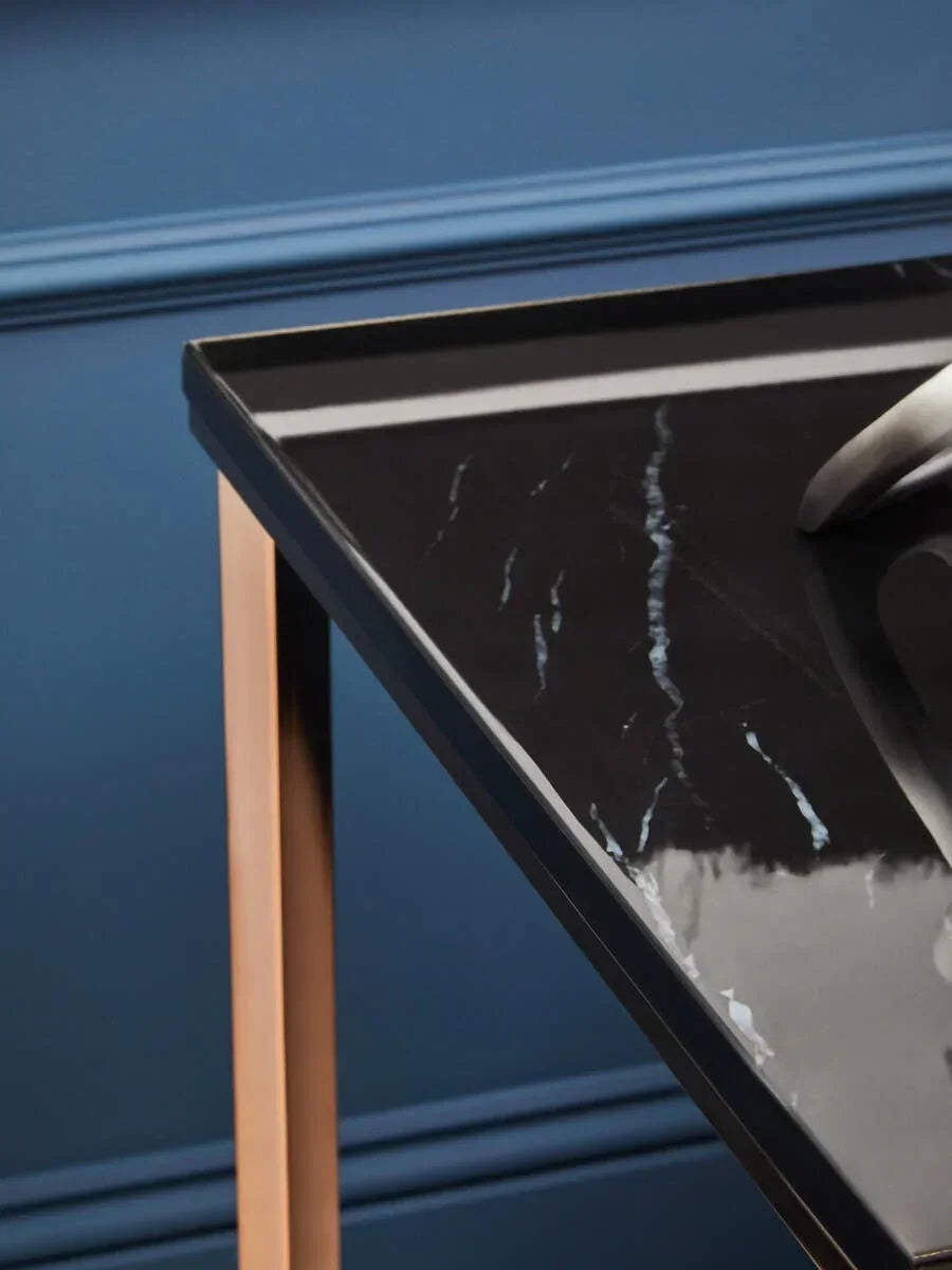 Close up of black marble top table with gold metal legs against blue wall