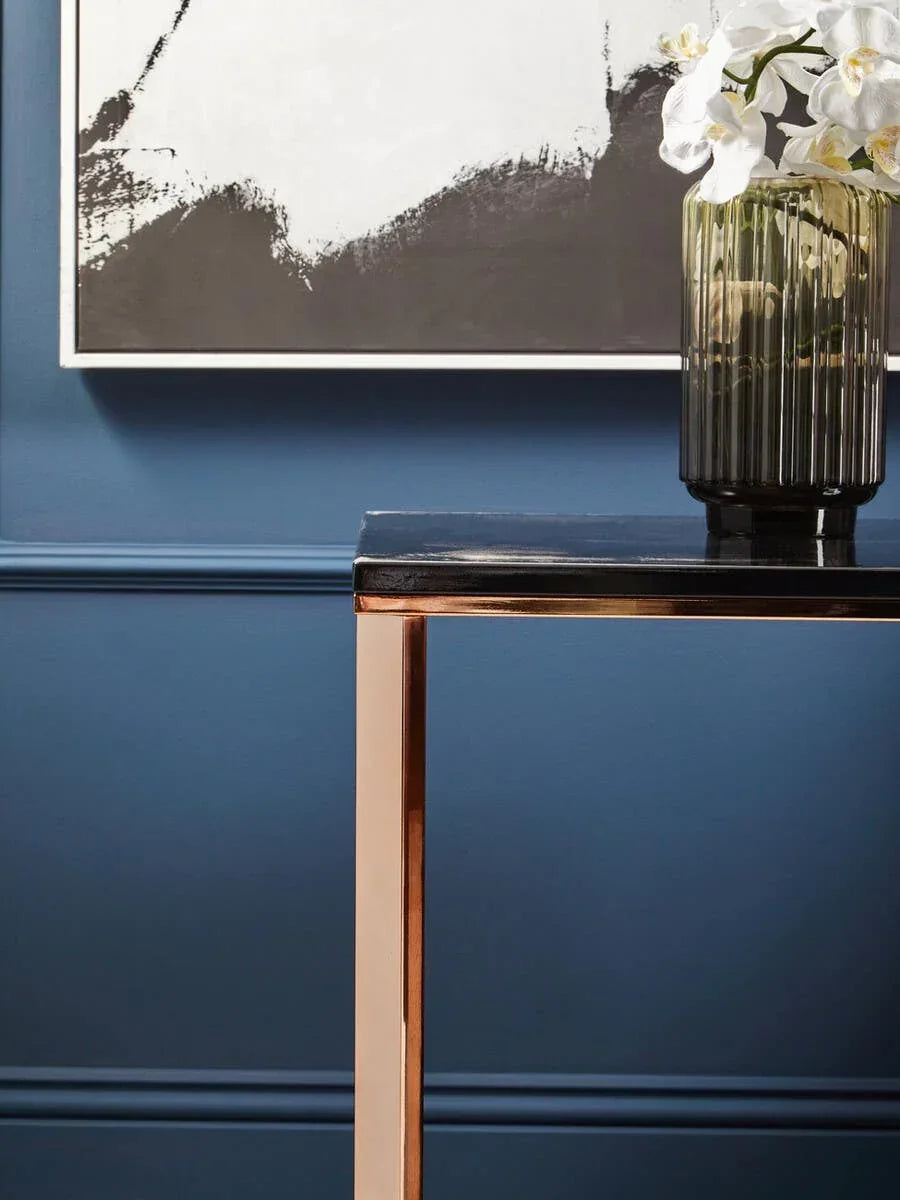 Contemporary console table with black glass top and gold metal legs against blue wall