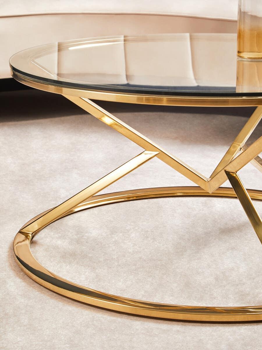 Round glass coffee table with gold metal frame on light carpet