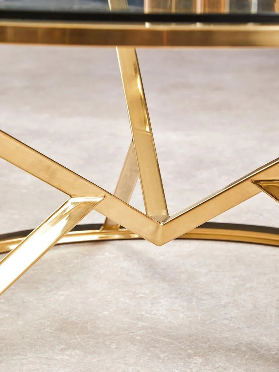 Glass coffee table with gold metal frame and geometric base on light floor