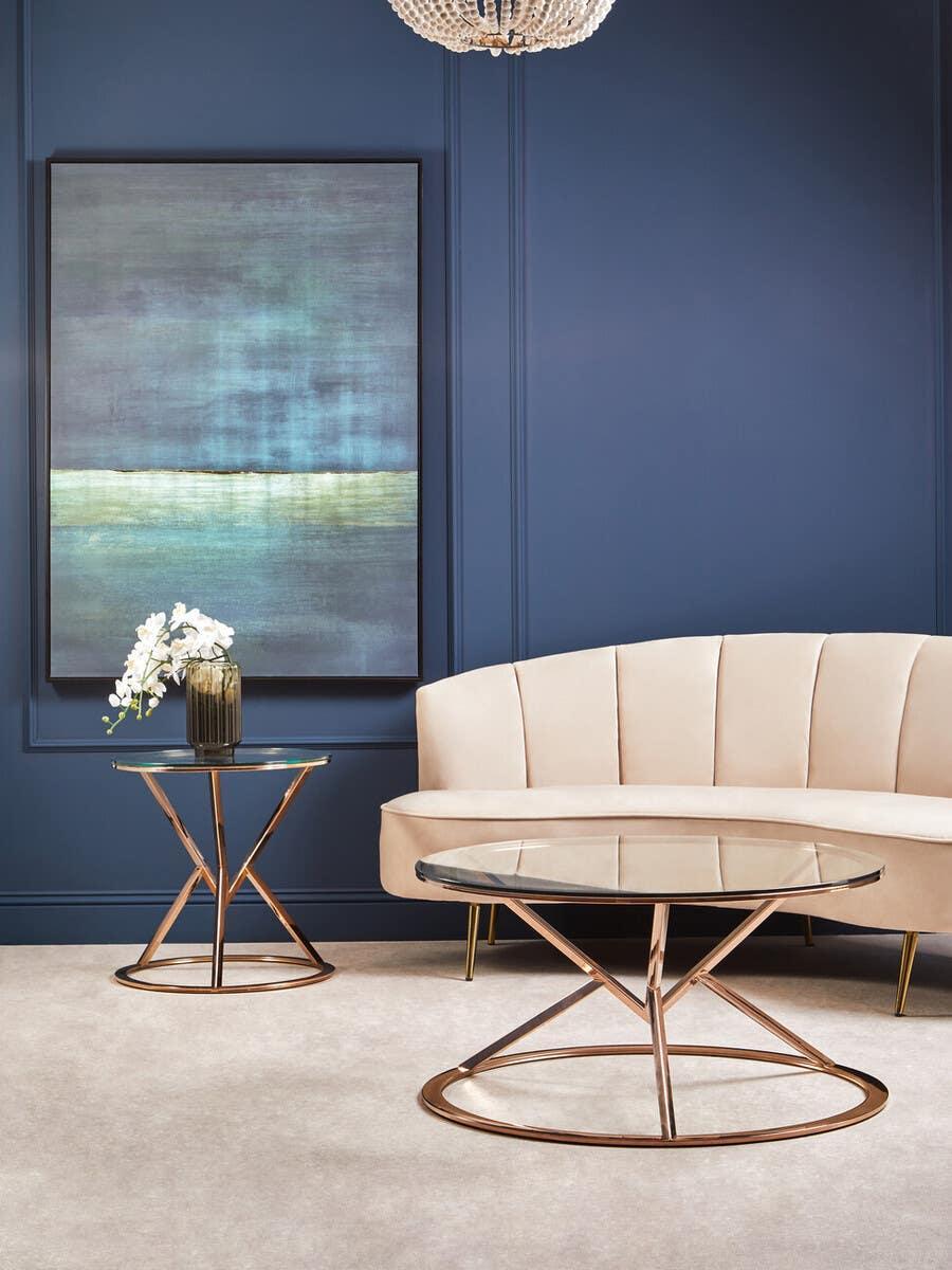 Glass coffee table with gold metal frame beside cream velvet sofa in modern living room