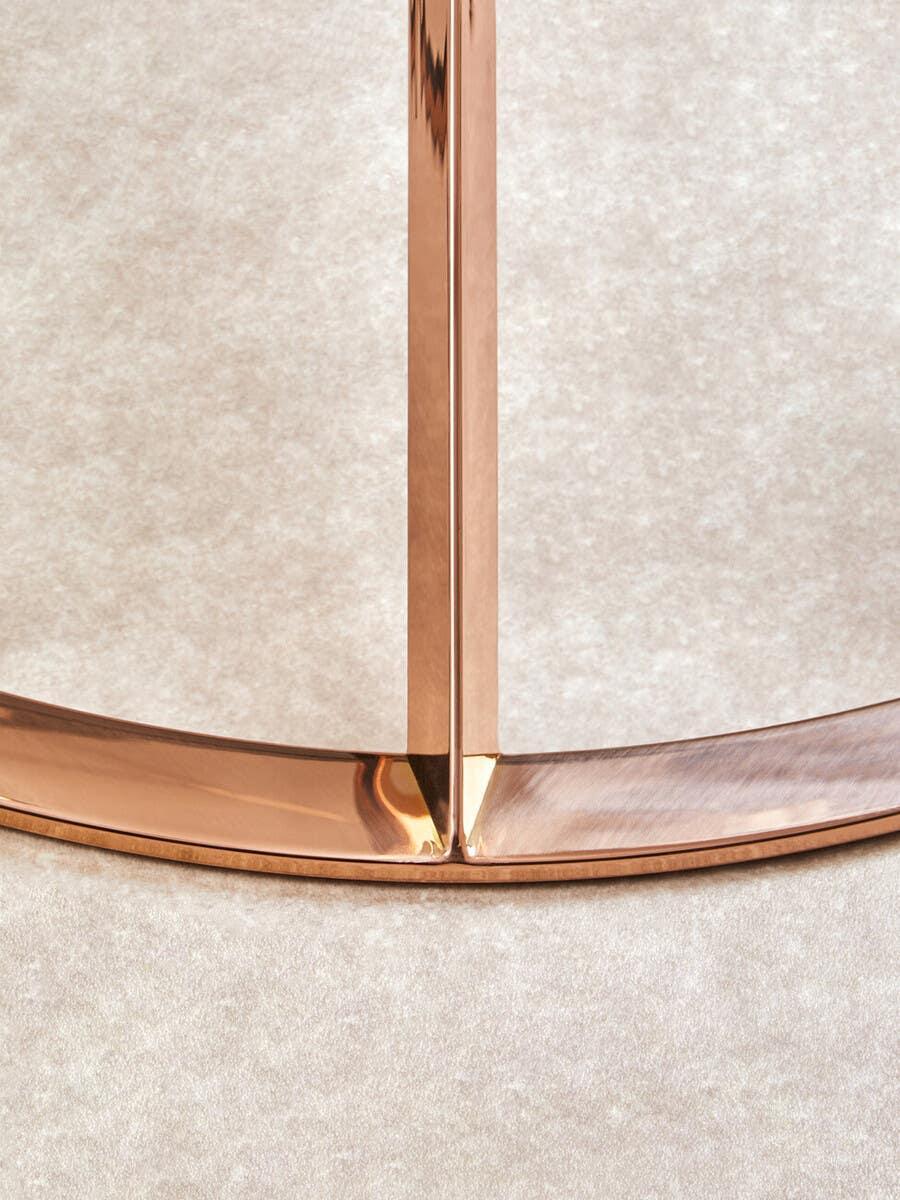 Closeup of gold metal table leg with curved base on beige carpet