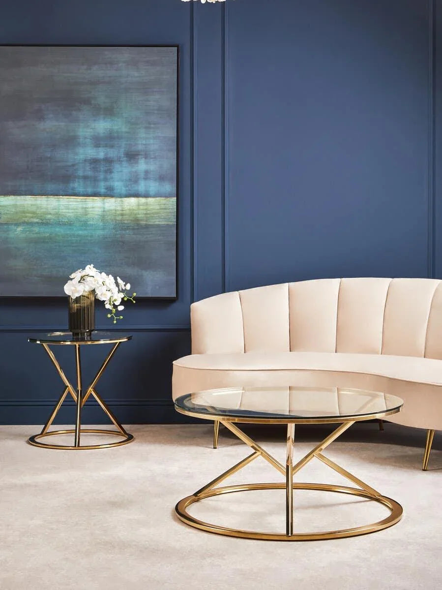 Glass coffee table with gold metal base beside cream velvet sofa in modern living room