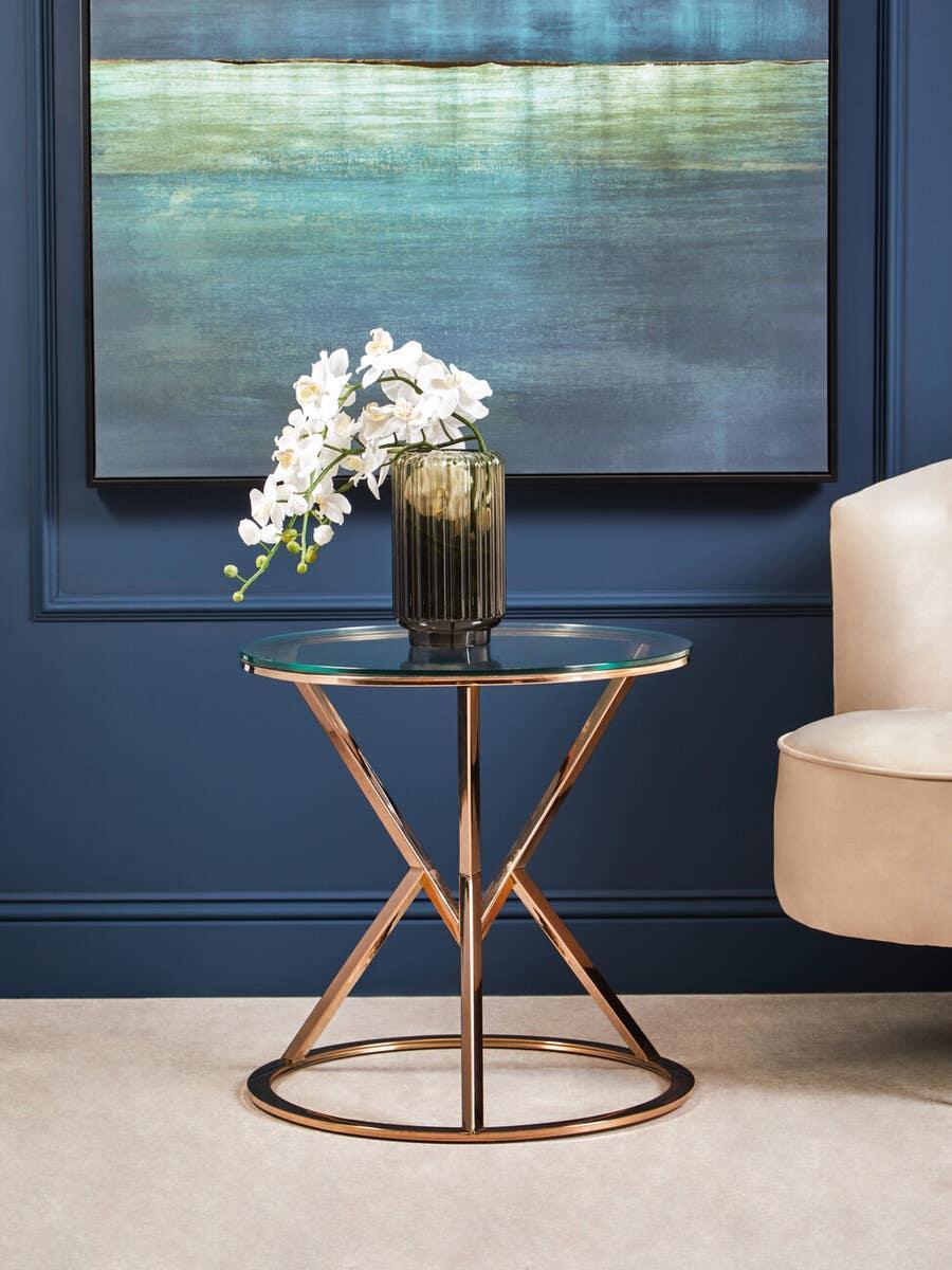 Glass top side table with gold metal base and vase of white flowers beside cream chair