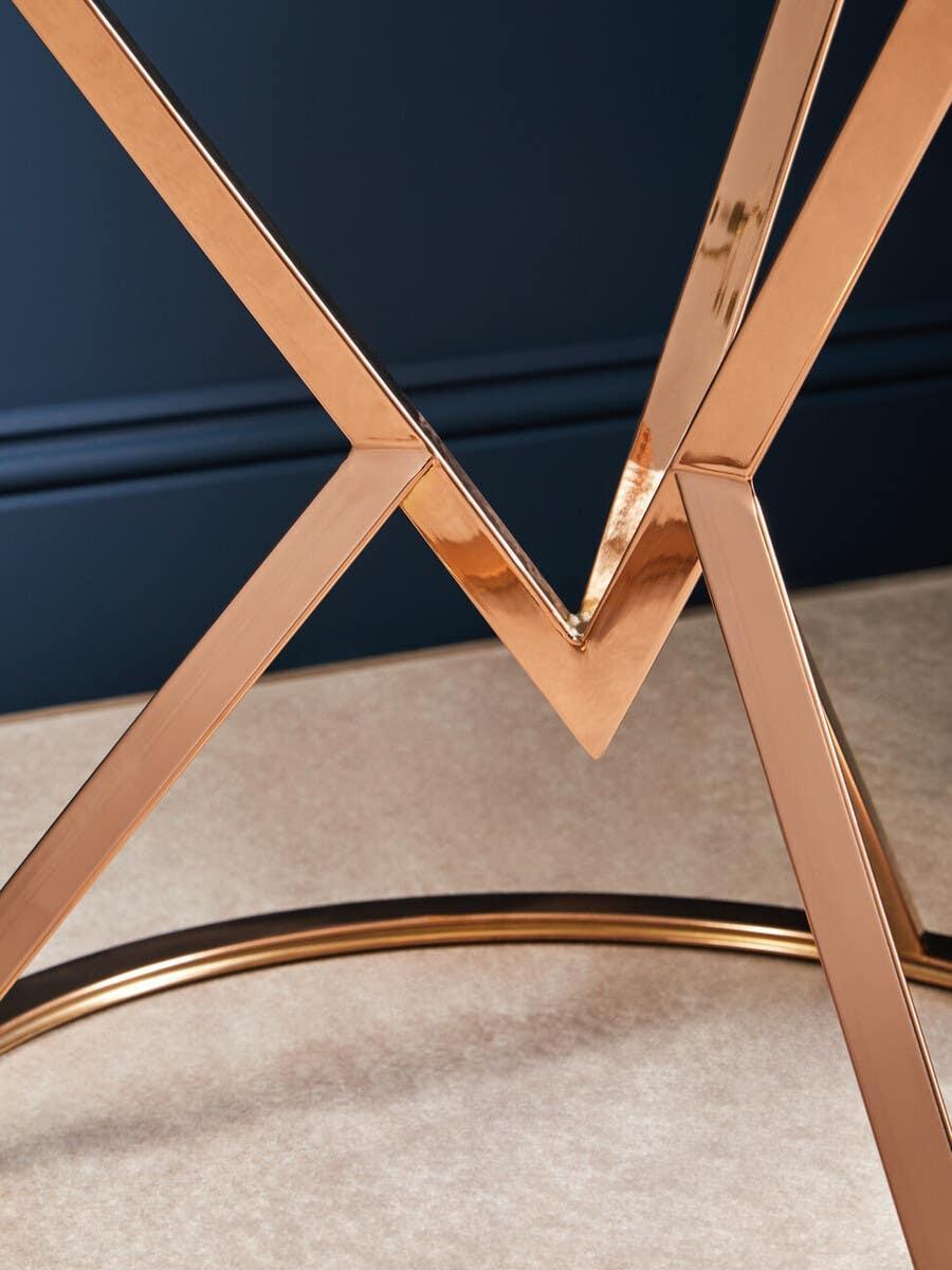 Close view of gold metal dining table legs with geometric cross design on carpet