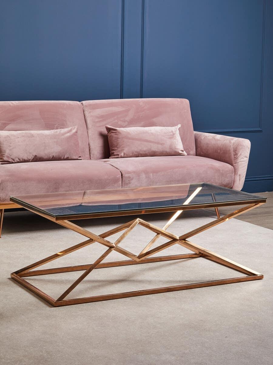 Glass top coffee table with gold geometric metal base in front of pink velvet sofa