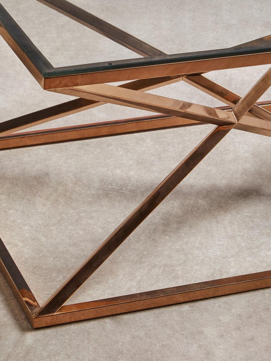 Glass coffee table with gold metal geometric base on beige carpet