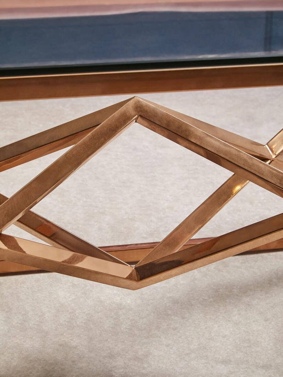 Geometric gold metal coffee table base with glass top on beige carpet