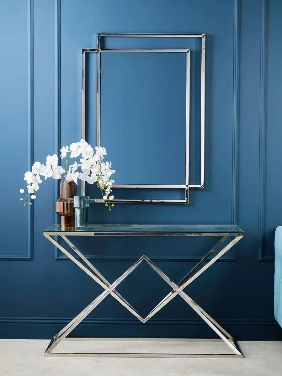 Glass console table with chrome frame and vases, orchid flowers, blue paneled wall
