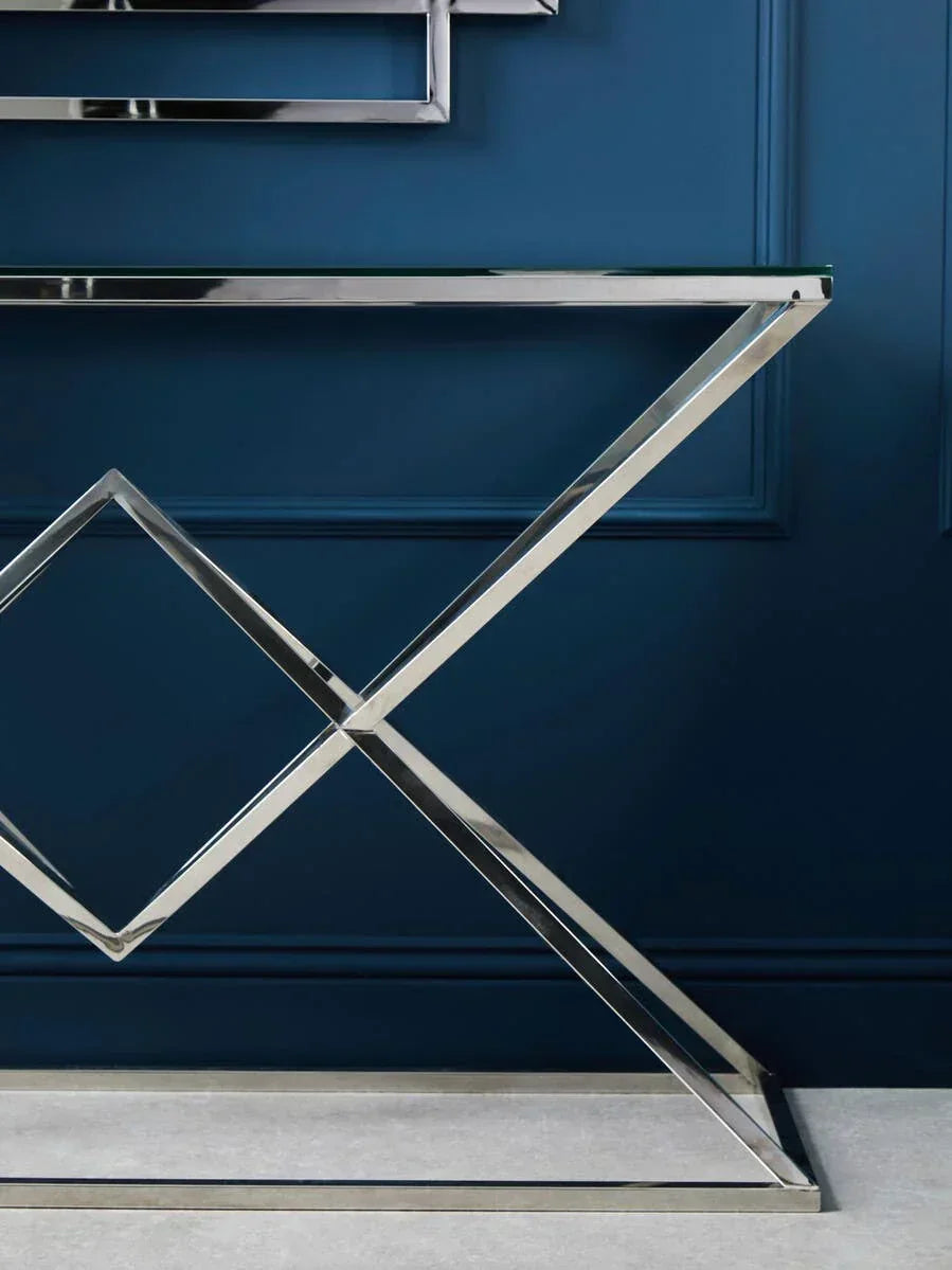 Chrome console table with glass top and geometric metal frame against blue wall