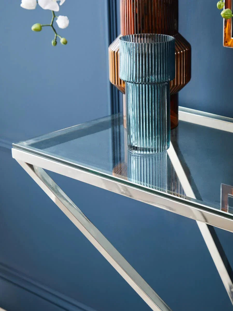 Glass console table with chrome legs and modern vases against blue wall