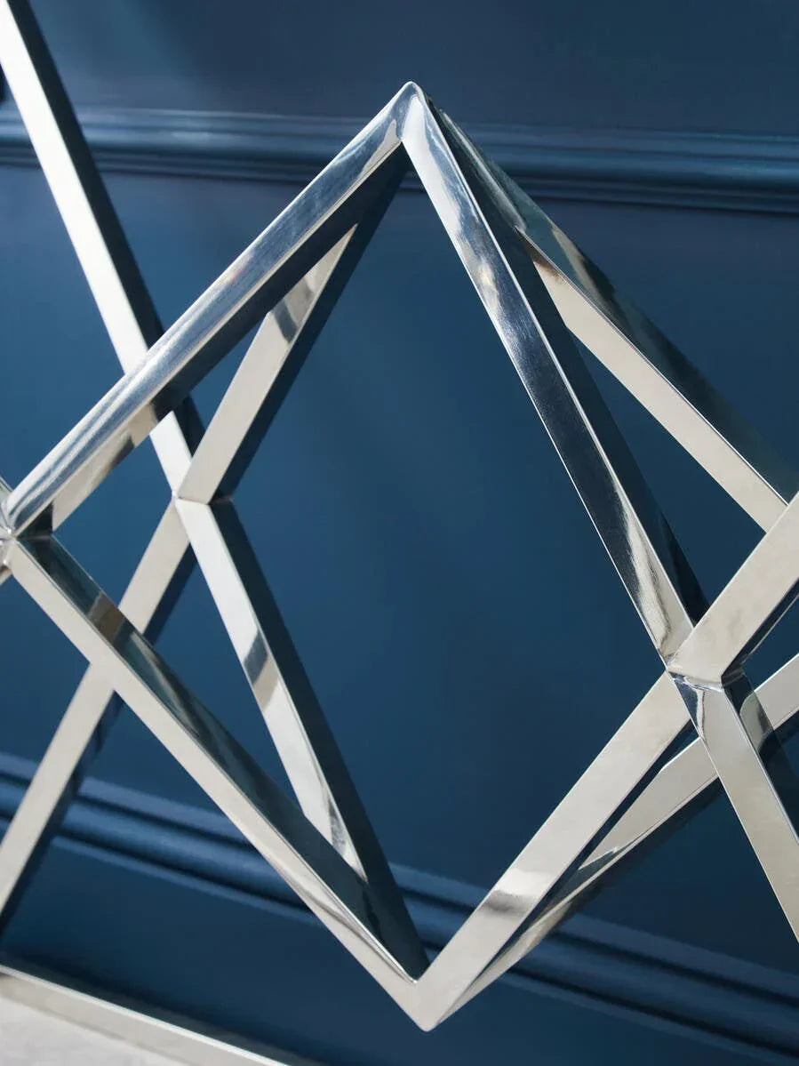 Geometric chrome table base with diamond pattern against dark blue wall