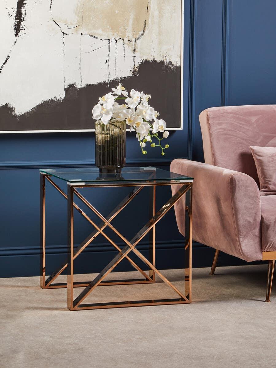 Glass top side table with gold metal frame beside pink velvet armchair
