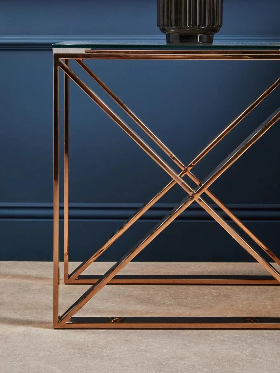 Glass console table with gold geometric metal frame against navy wall