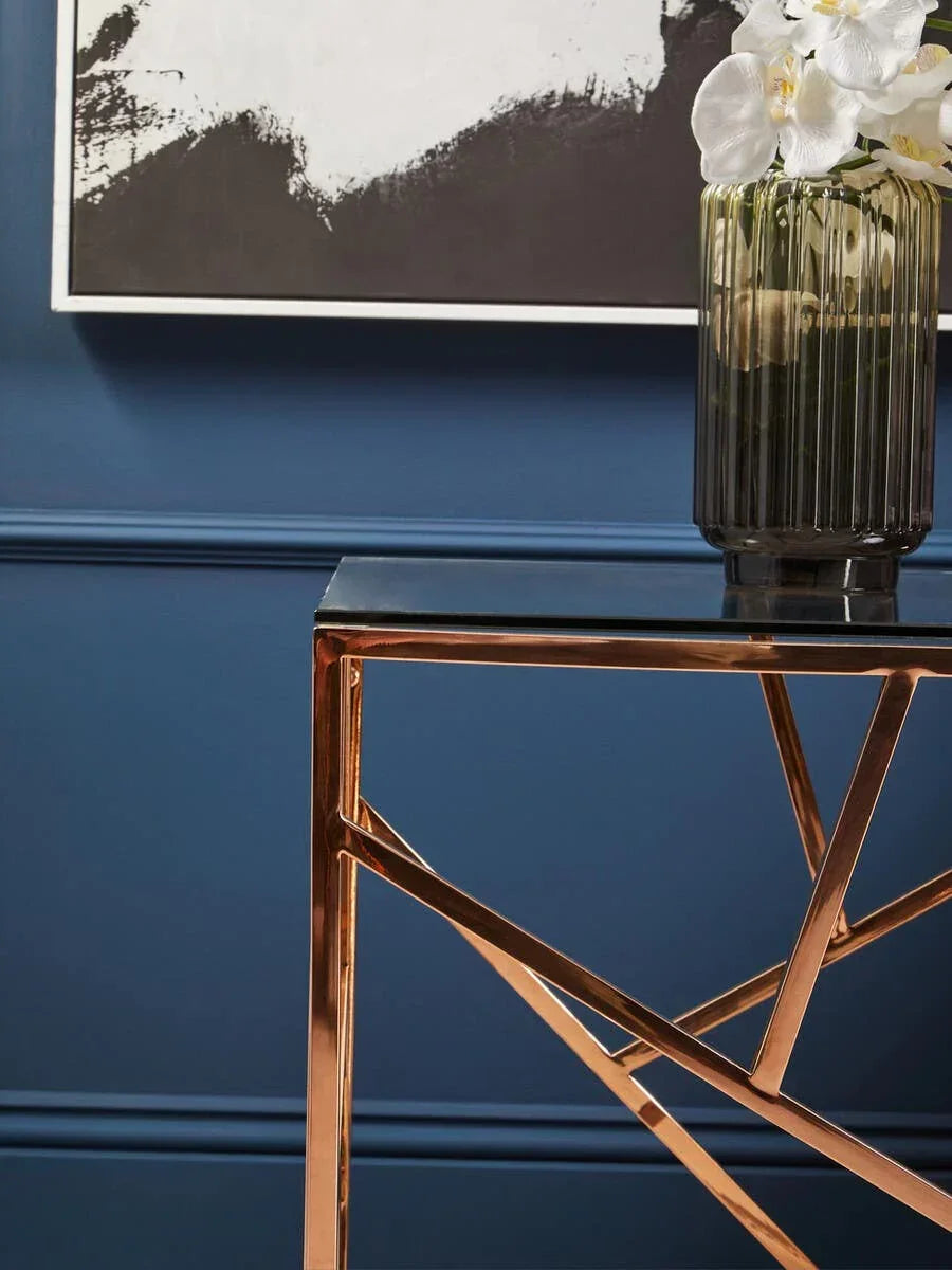 Modern console table with gold metal frame and black glass top against blue wall