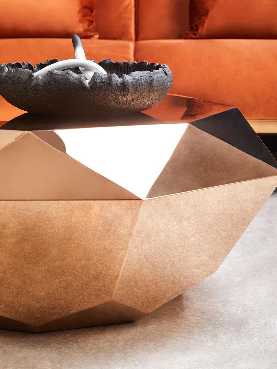 Geometric gold coffee table with black decorative bowl in front of orange velvet sofa