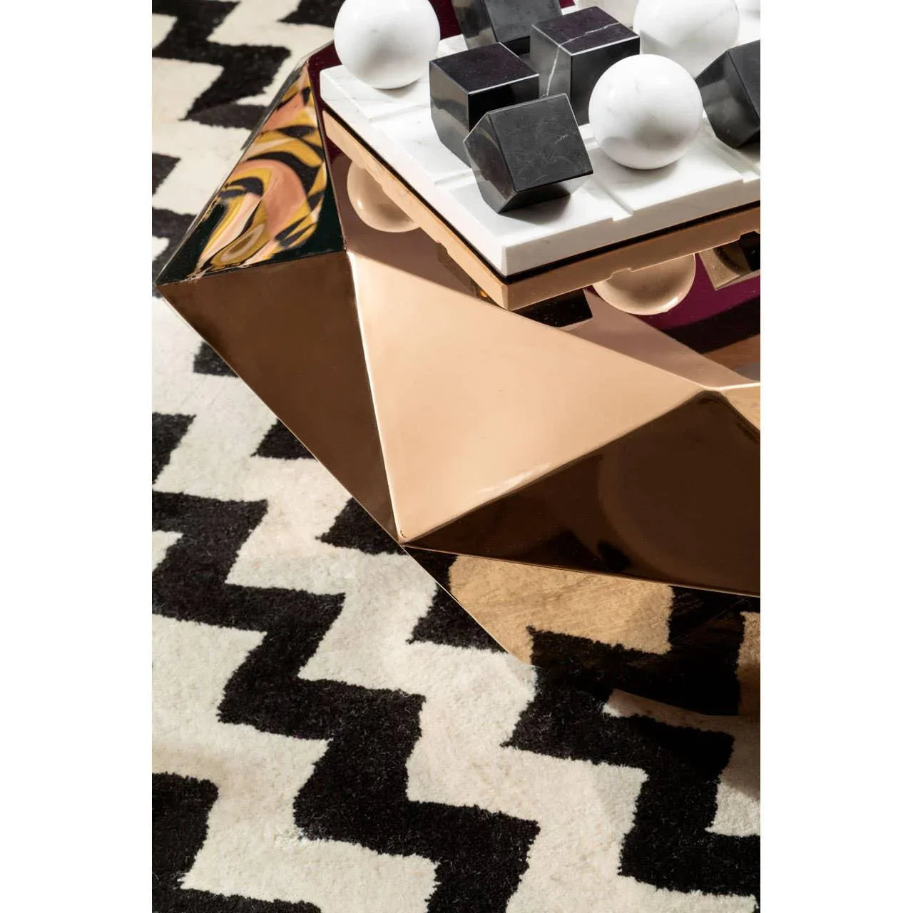 Geometric gold coffee table on black and white zigzag rug with decorative marble accents