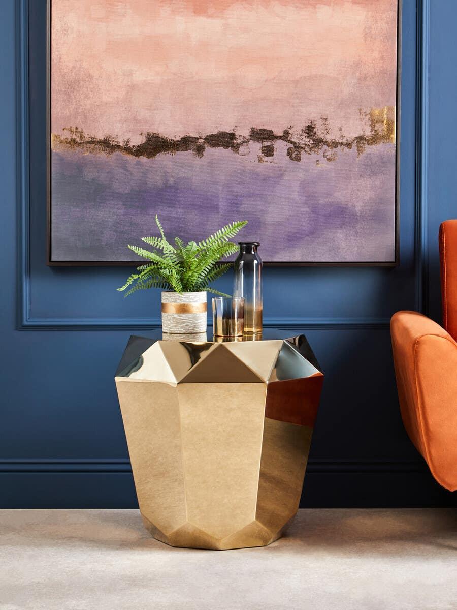 Gold geometric side table with a plant and glass decor, placed beside an orange chair