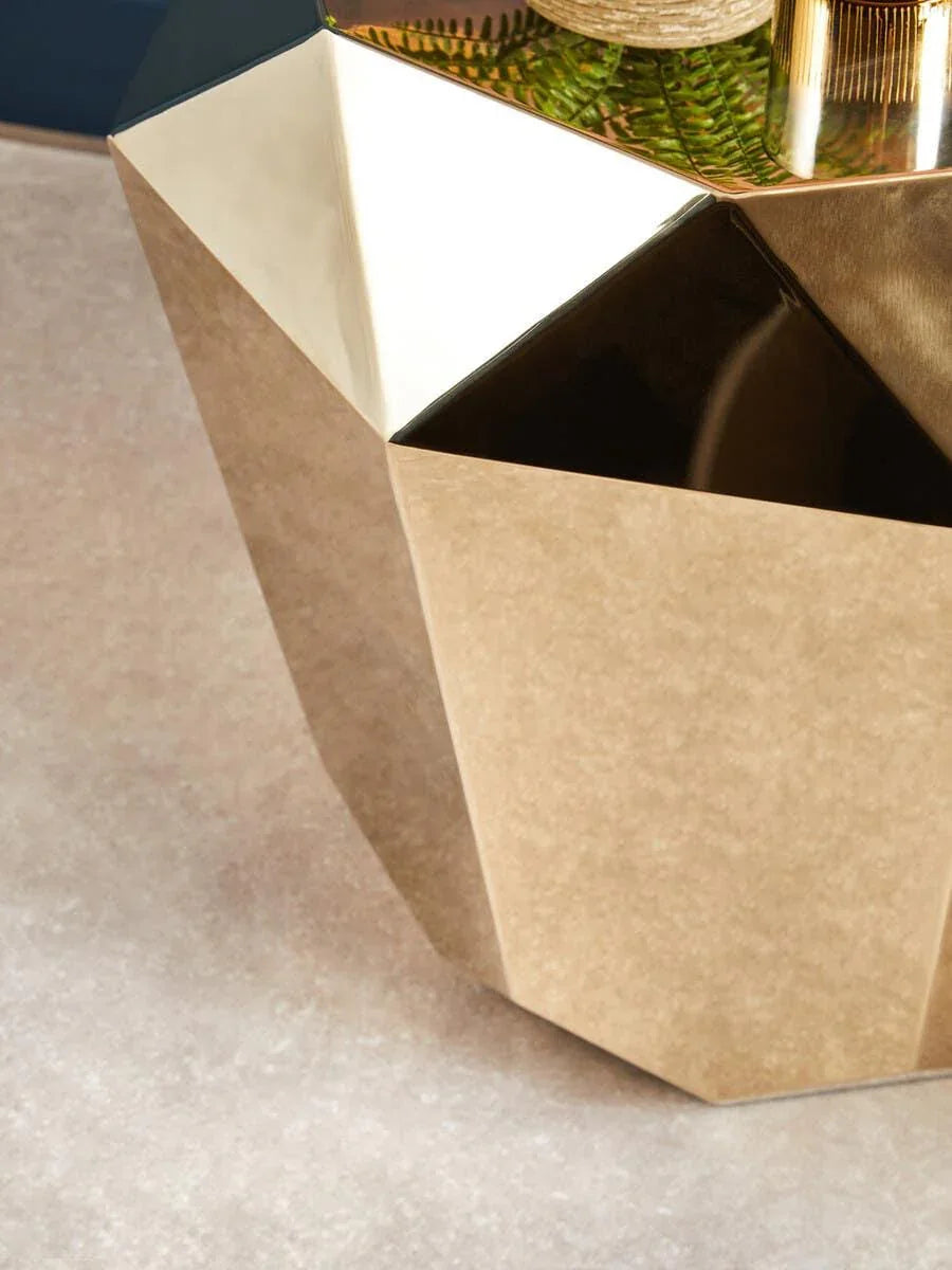 Geometric gold side table with mirrored top and plant decor, close-up corner view