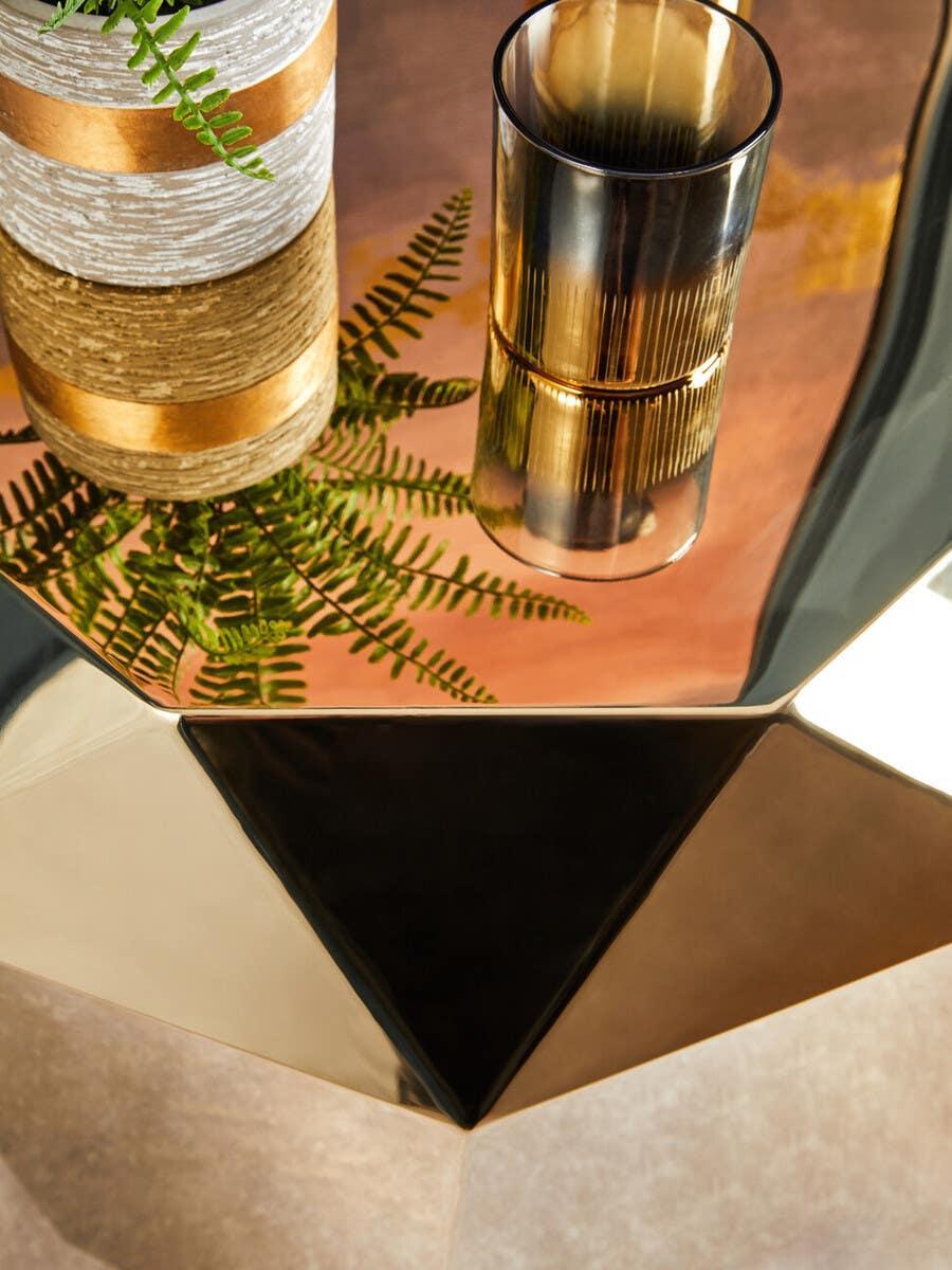 Geometric gold coffee table with glass vase and potted plant on reflective surface
