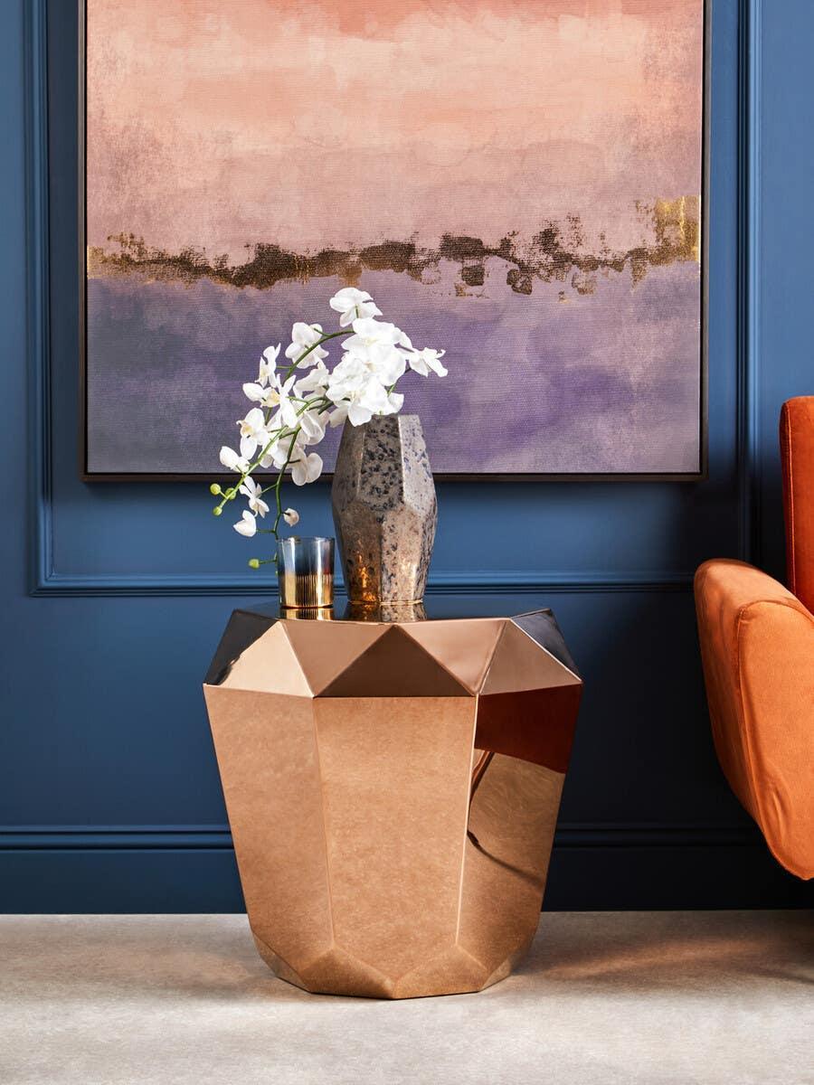 Geometric gold side table with decorative vases and flowers beside orange armchair