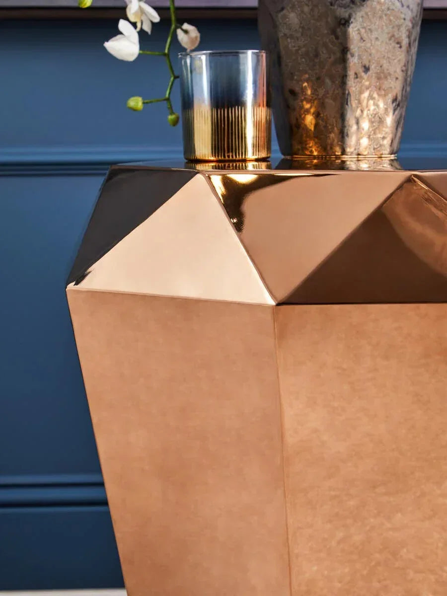 Geometric gold side table with metallic vase and glass tumbler against blue wall