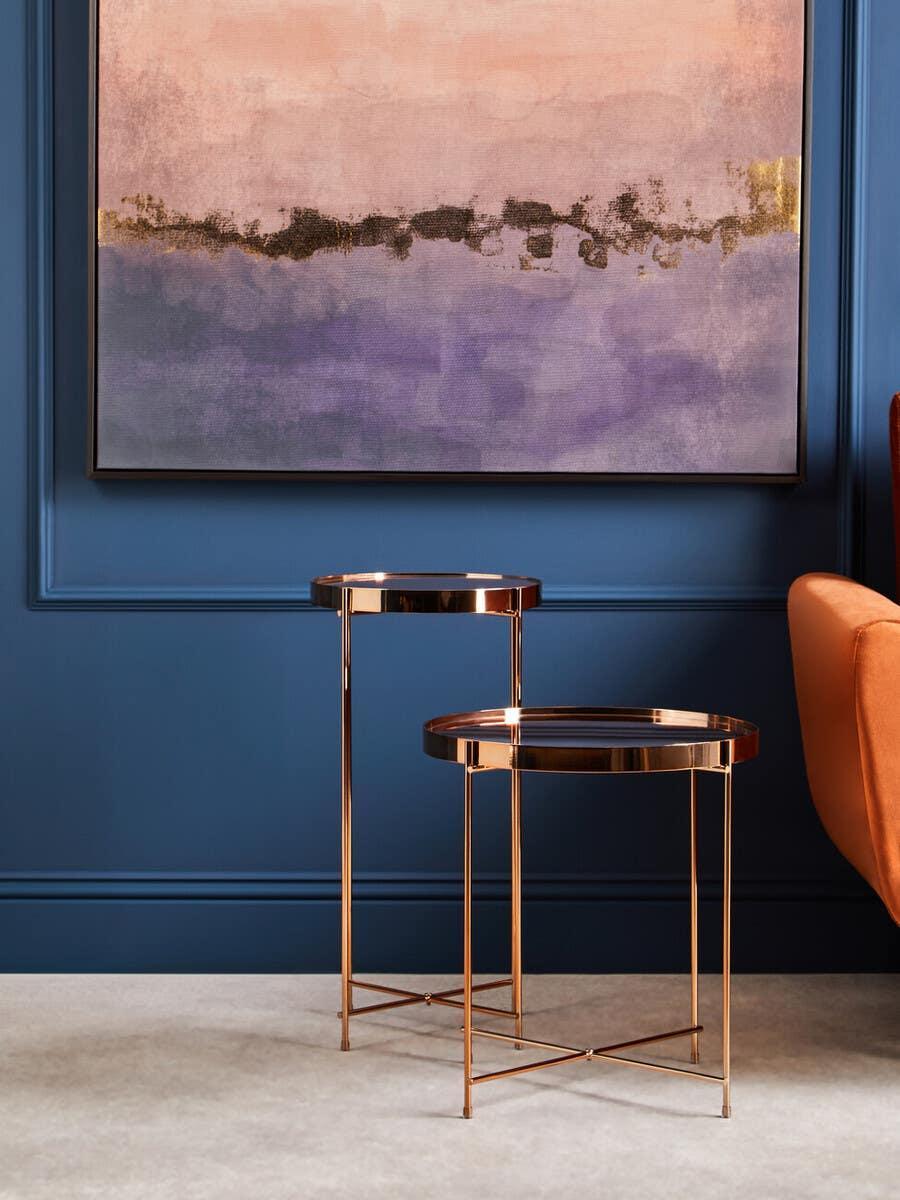 Set of two round gold metal side tables with mirrored tops against blue wall