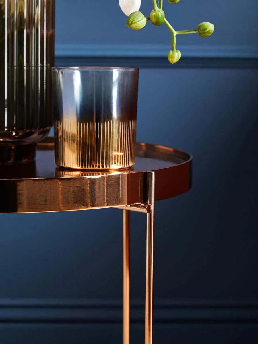 Round gold side table with metallic ribbed glass vase against blue wall