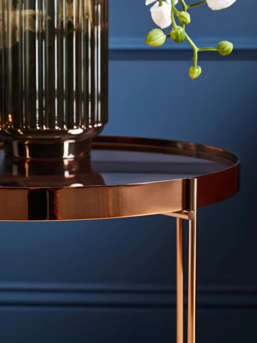 Round bronze metal side table with glass vase and white orchid flowers against blue wall
