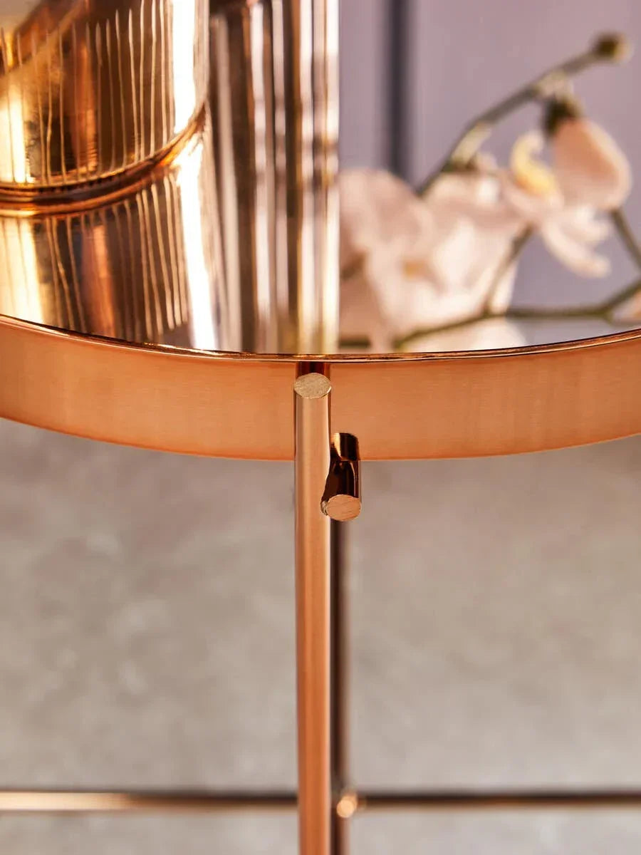Round gold metal side table with glass top and floral reflection in close-up view