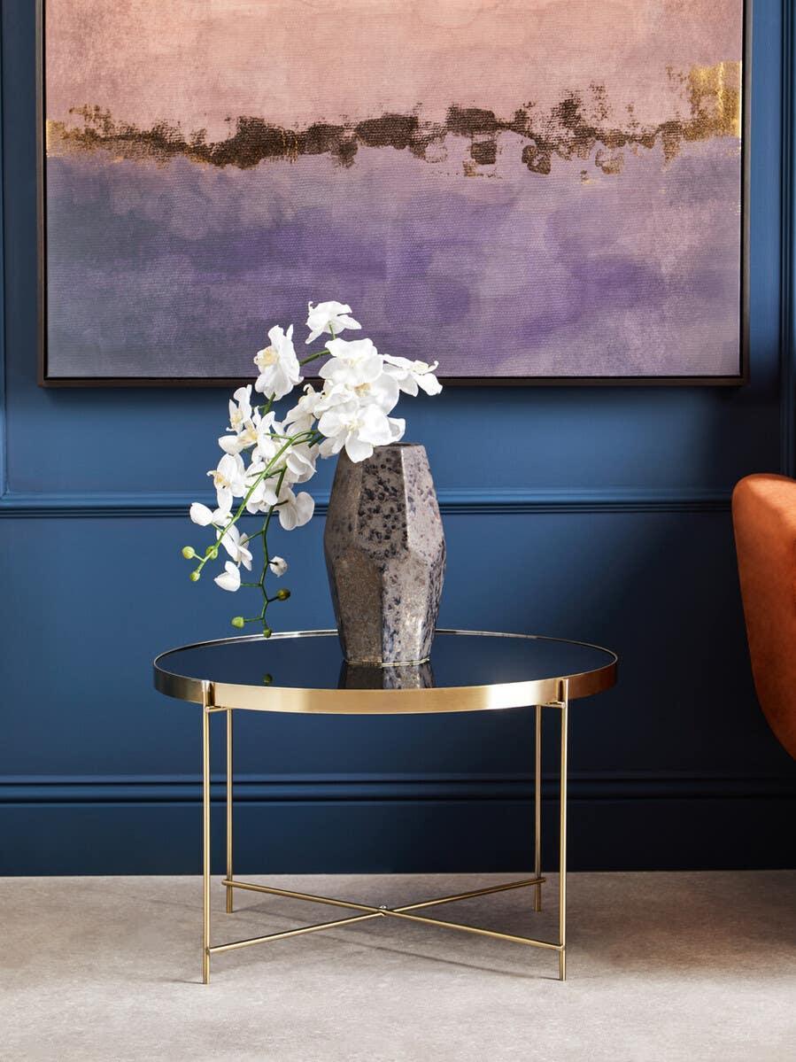 Gold round glass coffee table with modern vase and white flowers in stylish living room