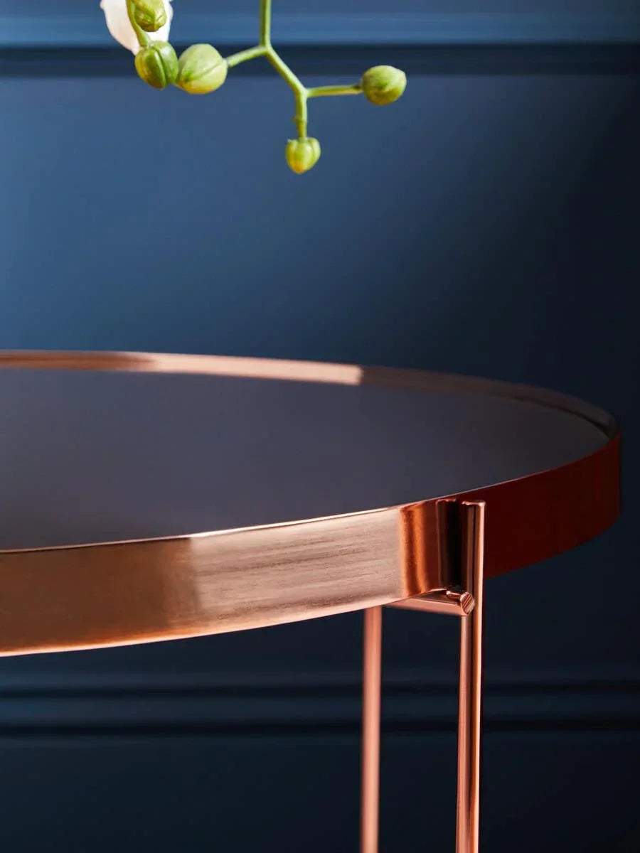 Round copper side table with sleek edge and metal legs against blue wall