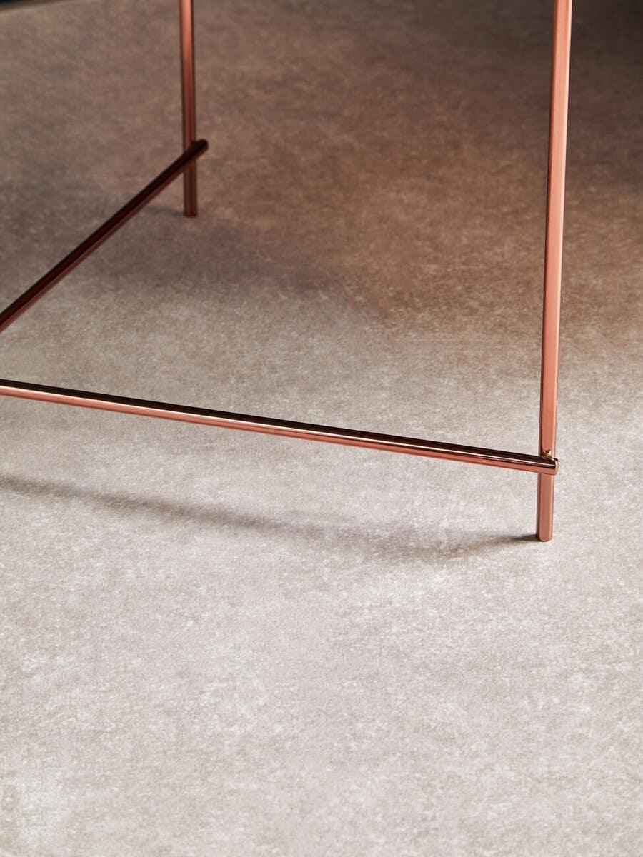 Copper metal table legs with crossbar on a textured stone floor