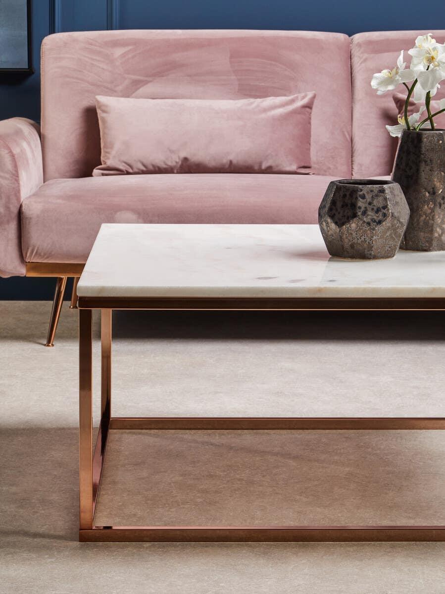 Velvet pink sofa with matching cushion behind marble top coffee table and ceramic vases