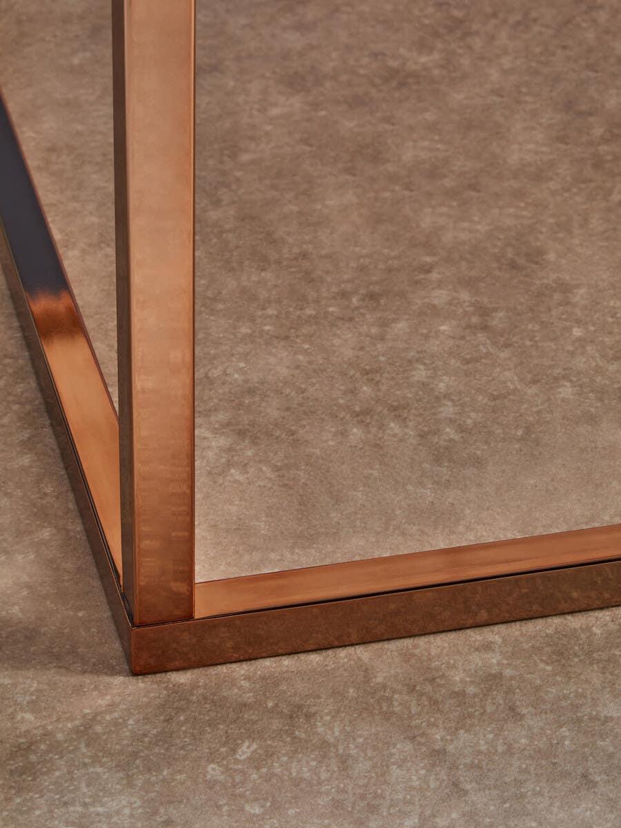 Copper metal table leg frame on textured beige floor, close-up angle
