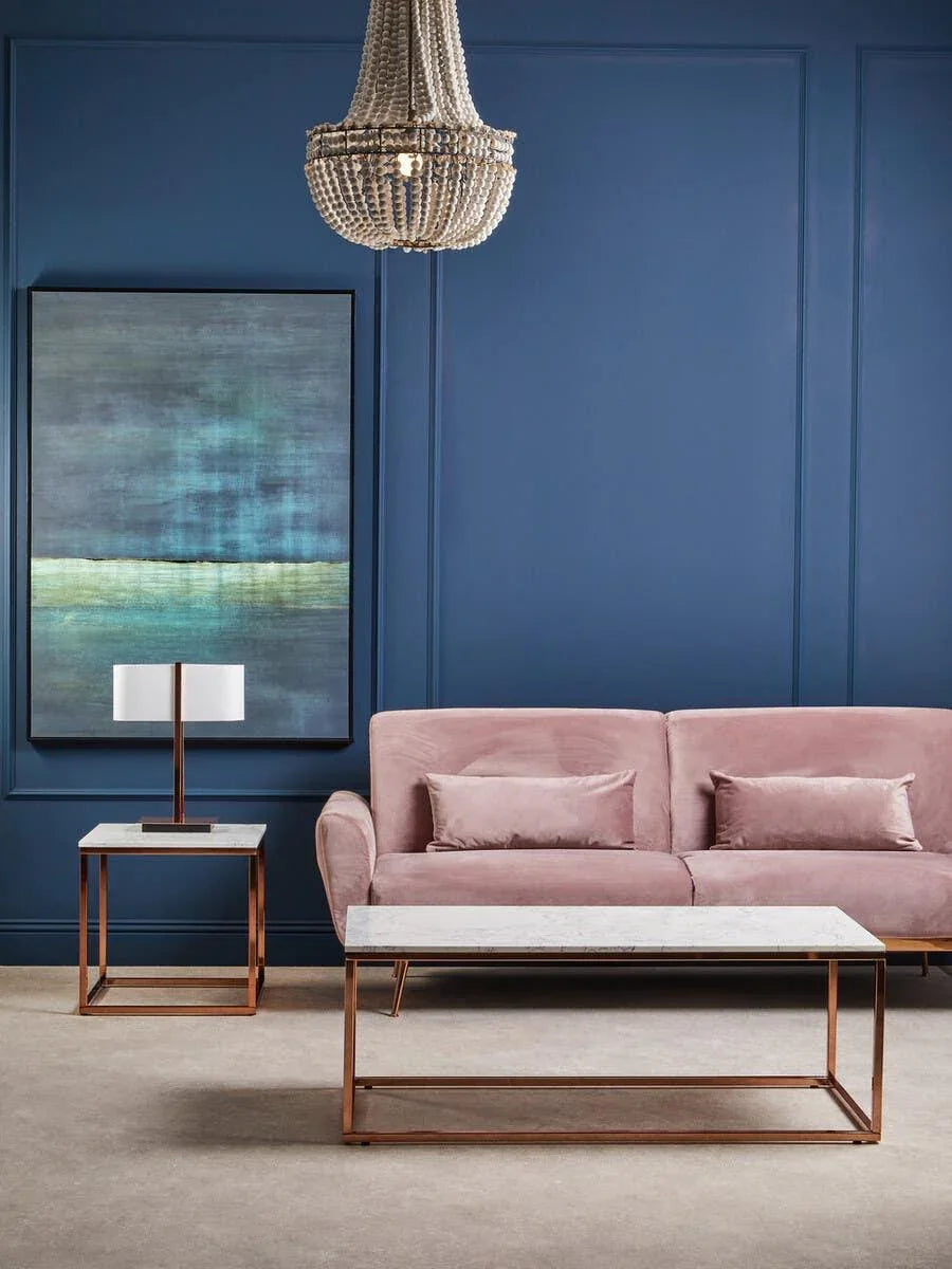 Blush pink velvet sofa with cushions, marble coffee table and lamp in blue living room