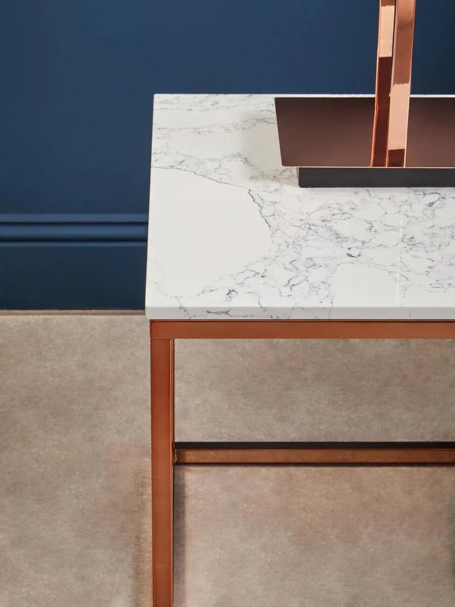 White marble top table with copper metal frame against blue wall and beige floor