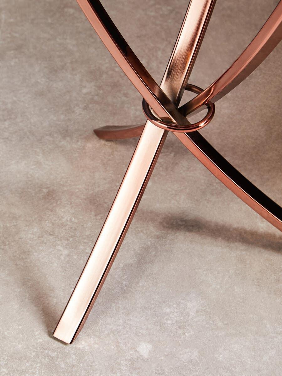 Rose gold metal table leg frame with crossed design on stone effect floor