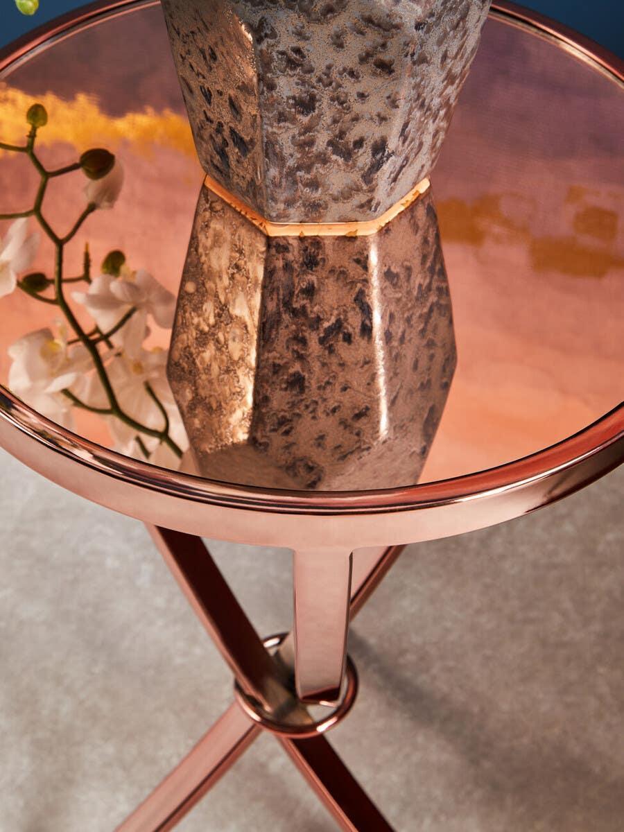 Round rose gold side table with mirrored top and decorative vase on carpeted floor