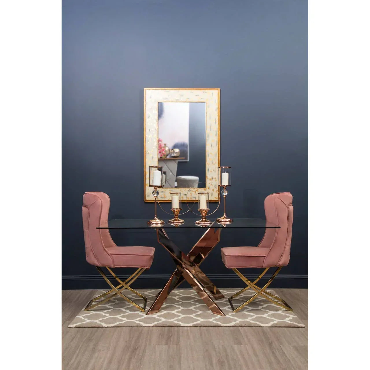 Glass dining table with rose gold base, two pink velvet chairs, modern mirror and candle holders