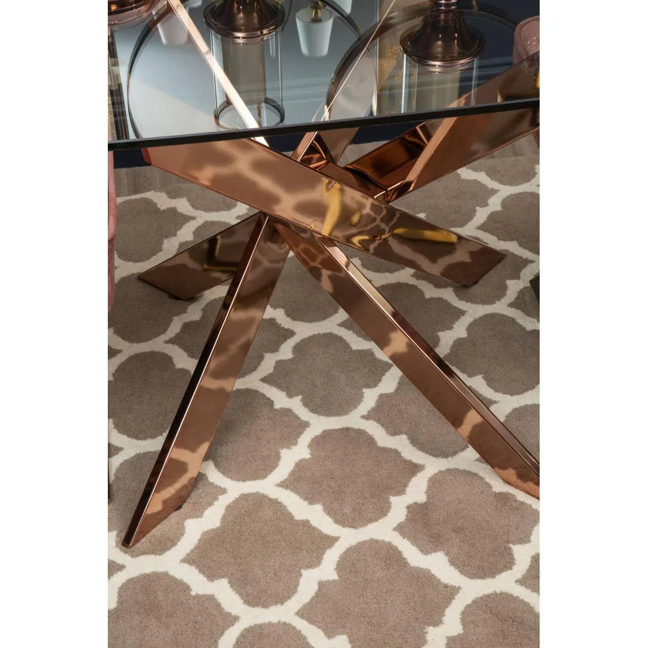 Glass dining table with rose gold metal legs on patterned beige rug