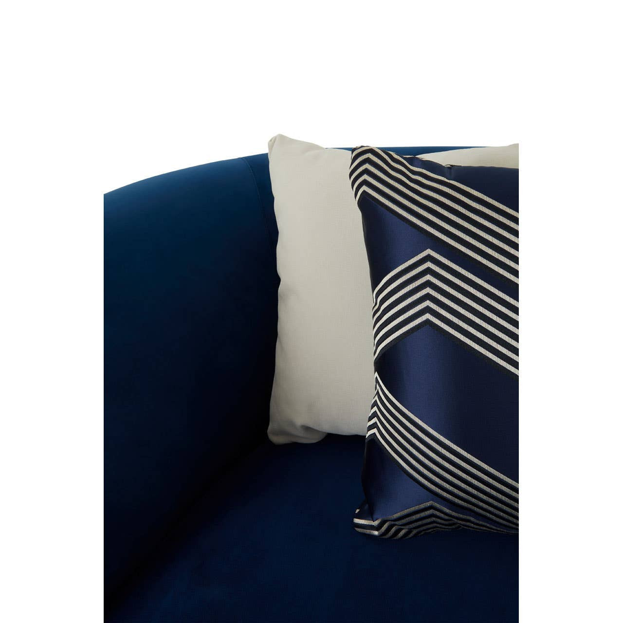 Dark blue velvet corner sofa with a plush texture, featuring a decorative pillow with a geometric pattern in shades of gray and navy. The sofa's armrest is visible, showcasing its modern design and comfortable seating