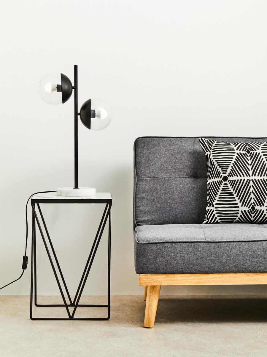 Grey fabric sofa with wooden legs and geometric cushion beside modern black metal side table
