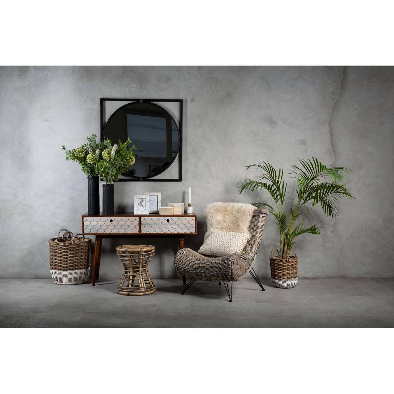 Rattan lounge chair with cushion, wicker stool, console table and indoor plants in modern living space