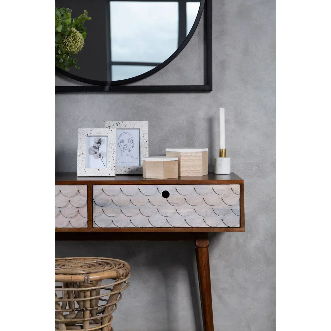Scalloped wood console table with two drawers, photo frames, boxes and a round wall mirror