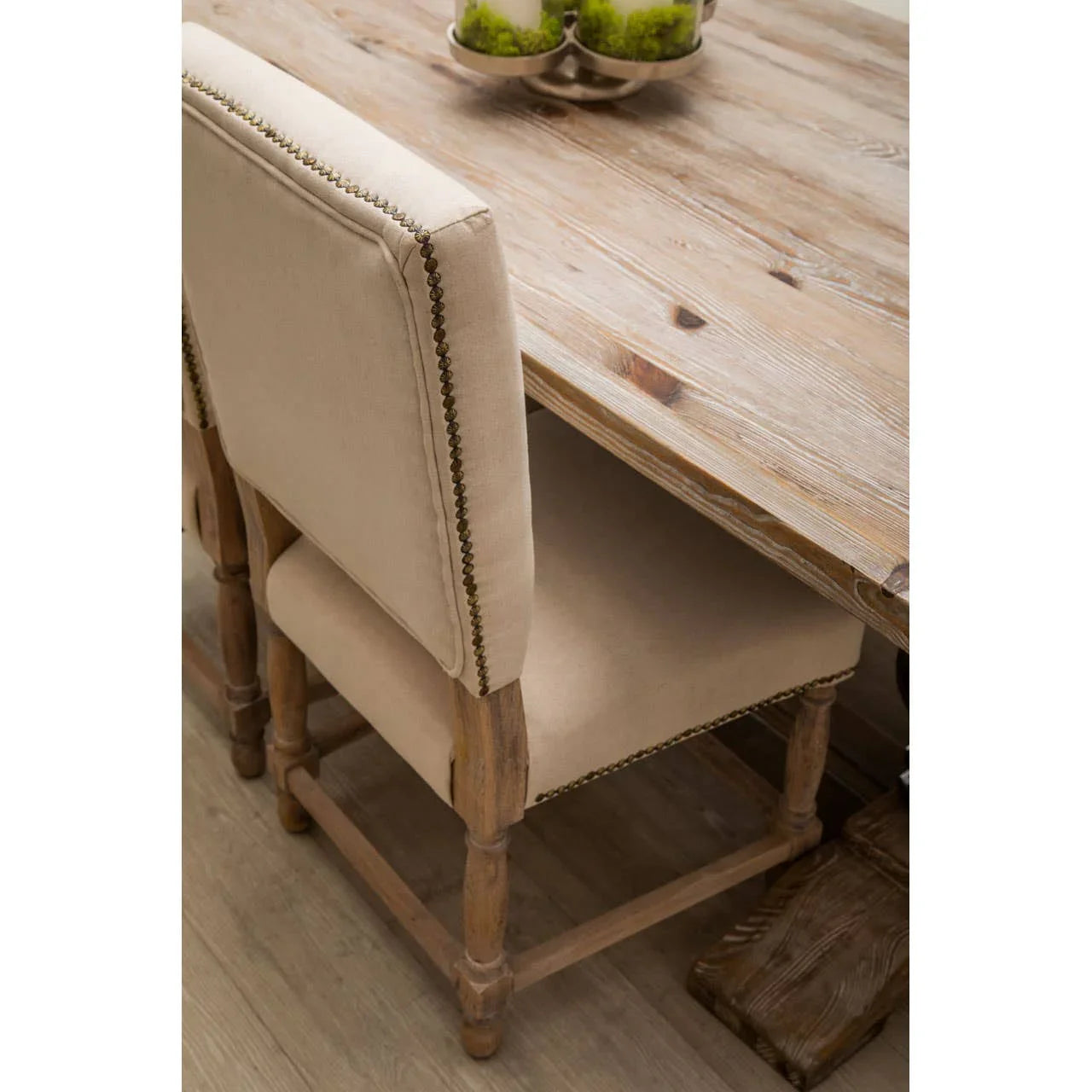 Beige upholstered dining chair with wood frame and nailhead trim at rustic dining table