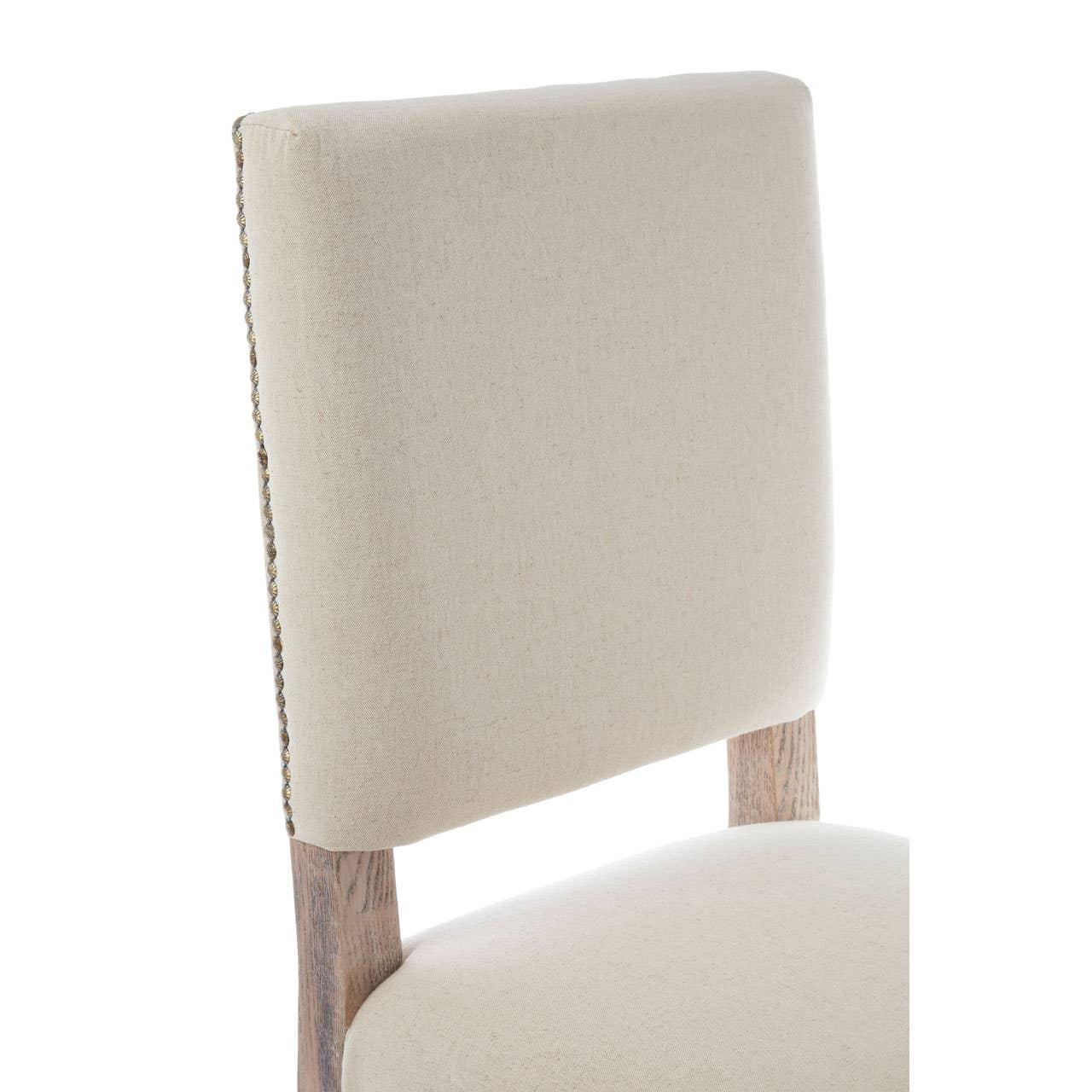 Beige upholstered dining chair with light wood frame and nailhead trim detail