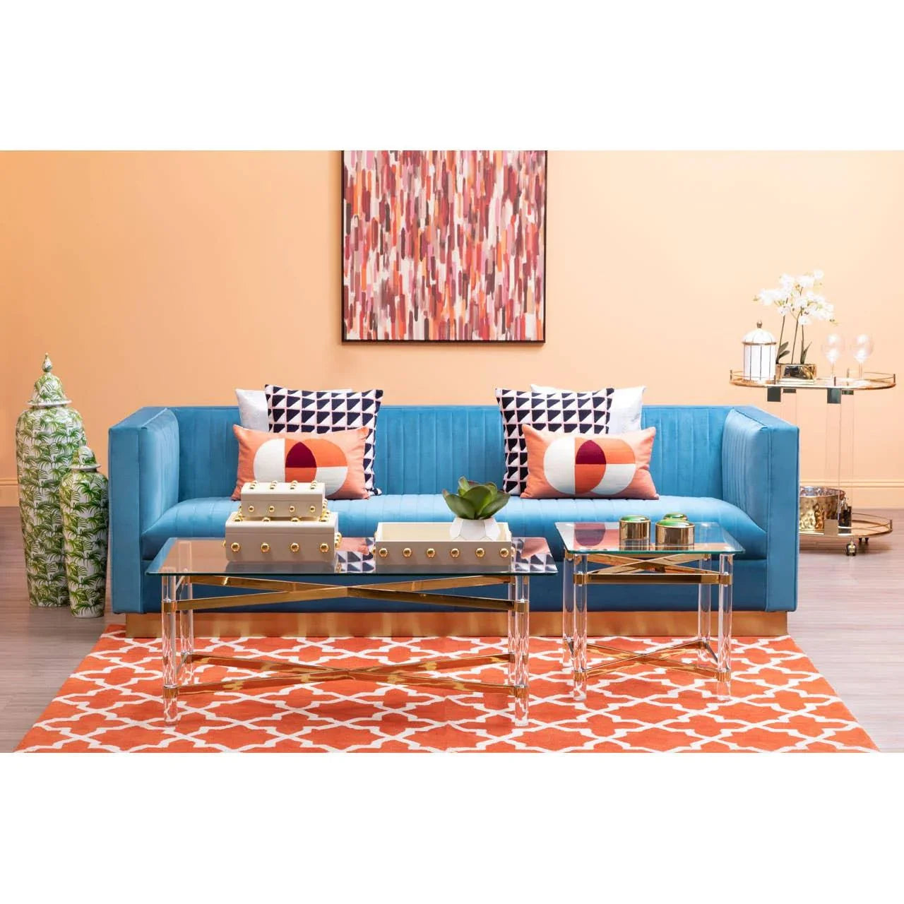 Blue velvet sofa with patterned cushions, glass coffee tables, and orange geometric rug