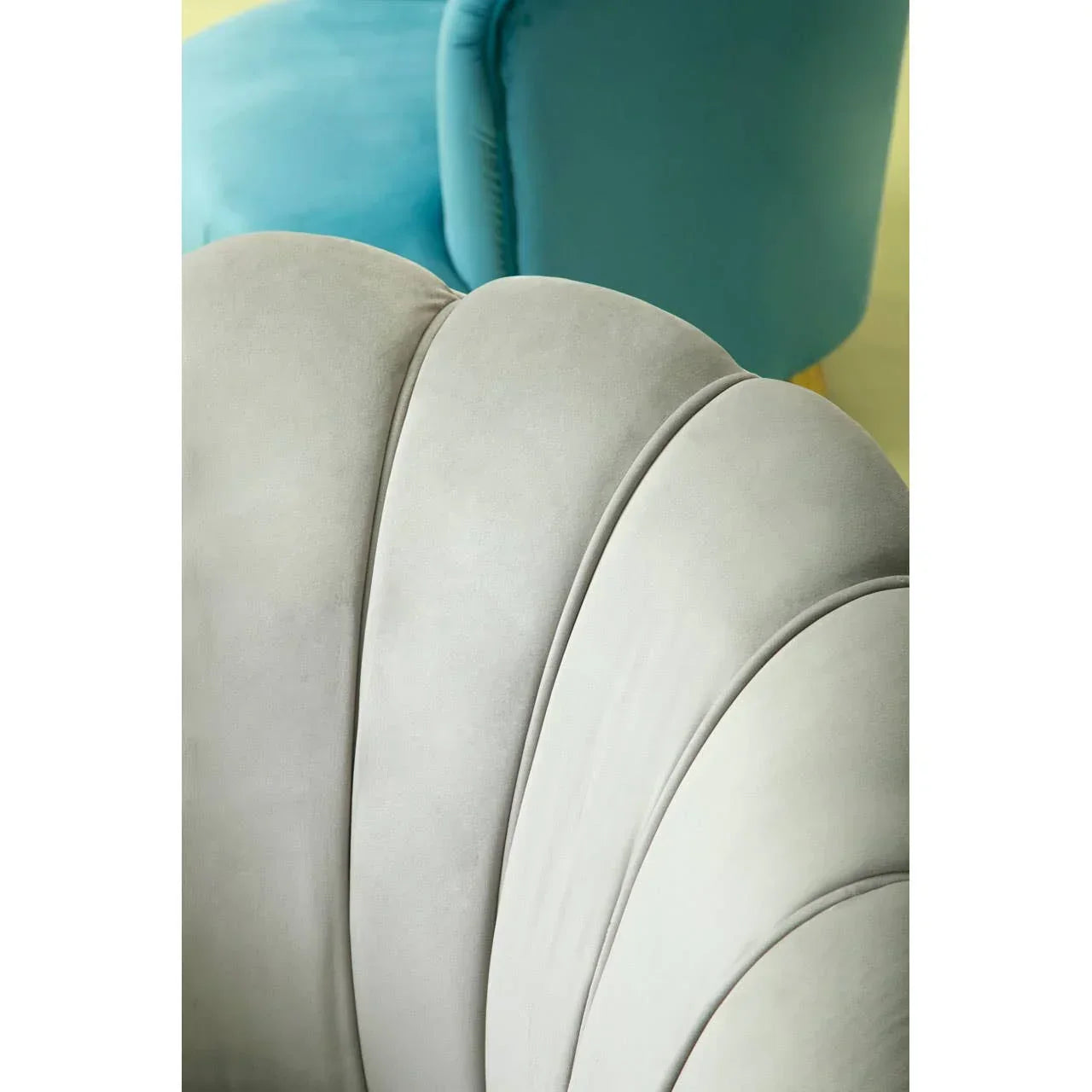 Closeup of grey velvet accent chair with scalloped backrest, blue armchair in background